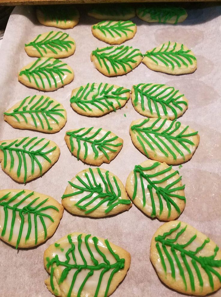 cookies decorated with green icing and leaves on a baking sheet, ready to go into the oven