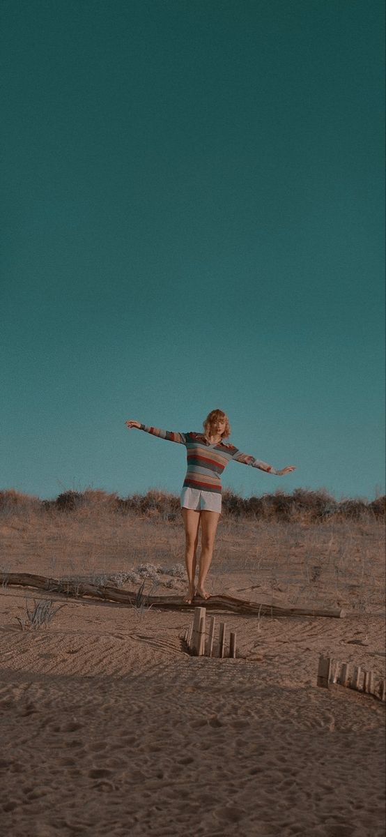 a woman standing on top of a sandy beach next to a blue and green sky