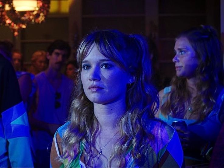 a woman standing in front of a group of people at a party with lights on