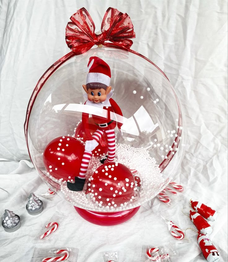 a glass ornament with an elf holding a heart in the center and candy canes around it