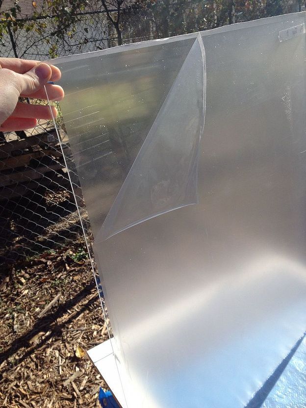 a person holding up a piece of clear plastic in front of a wire fence and tree