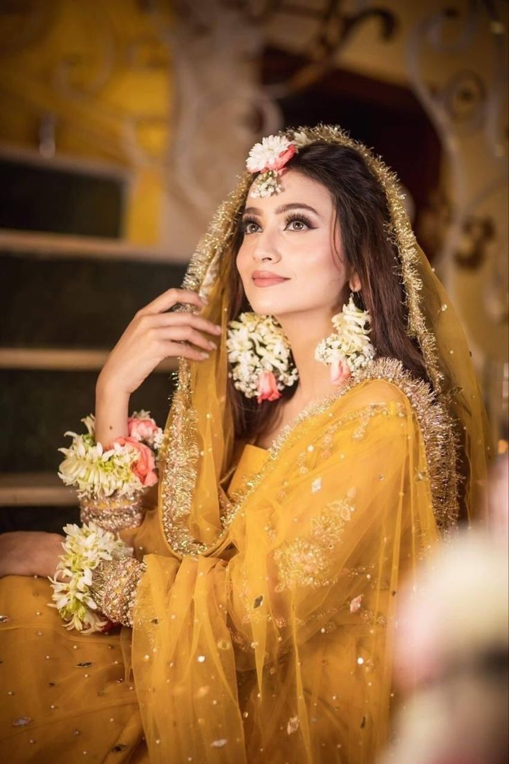 a woman wearing a yellow sari with flowers in her hair is posing for the camera