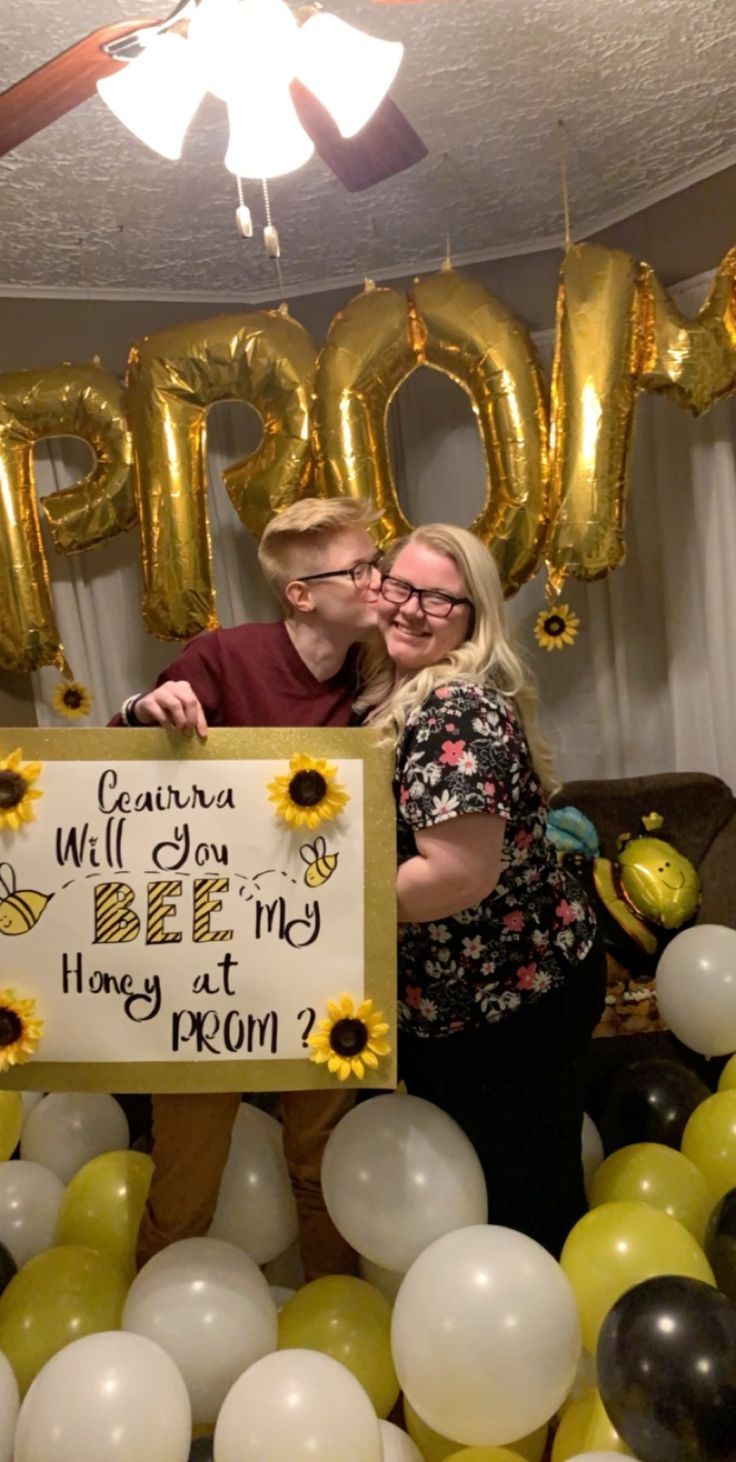 a man and woman holding up a sign in front of sunflowers with balloons