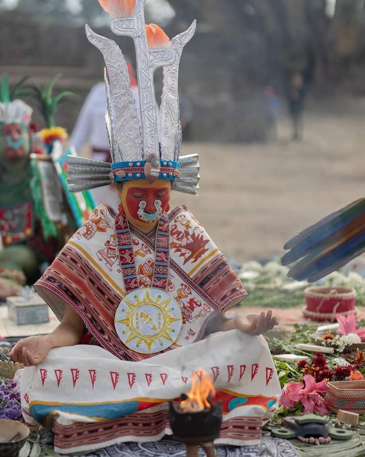 a person sitting on the ground in front of a fire pit with two large knives sticking out of it's head