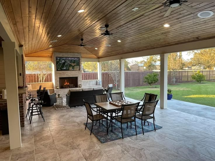 a covered patio with tables and chairs next to a fire place in the back yard