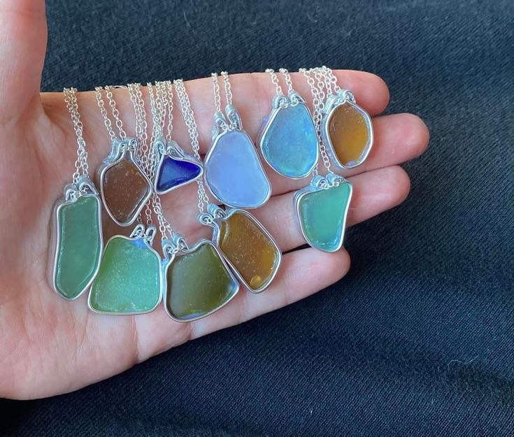 a person holding seven different colored sea glass pieces in their palm, with one being held by the other hand