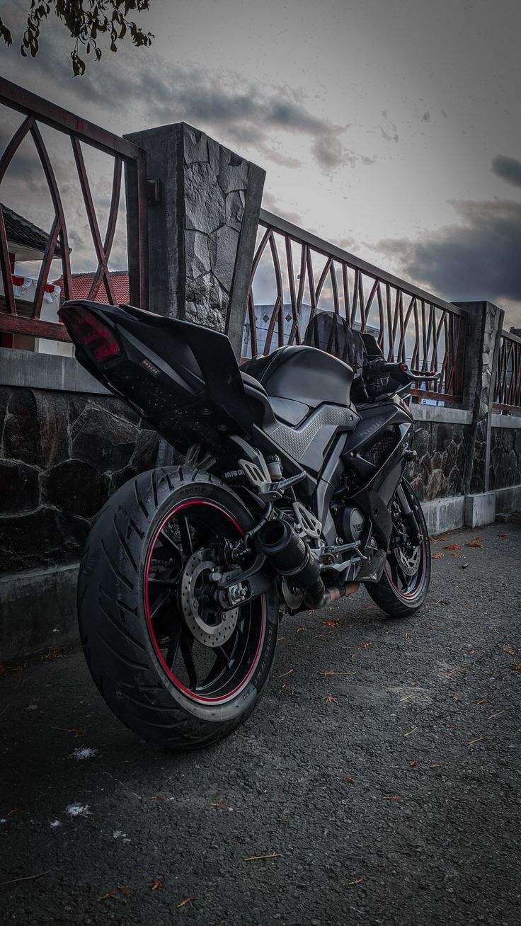 a black motorcycle parked on the side of a road near a stone wall with a bridge in the background