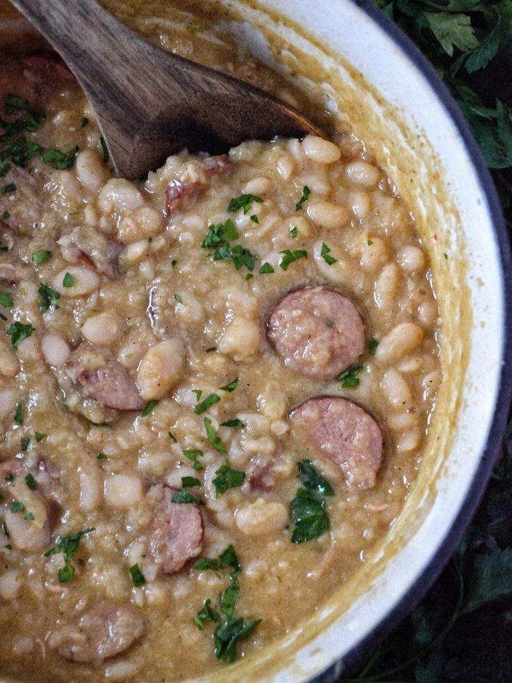 a pot filled with beans, sausage and parsley on top of a wooden spoon