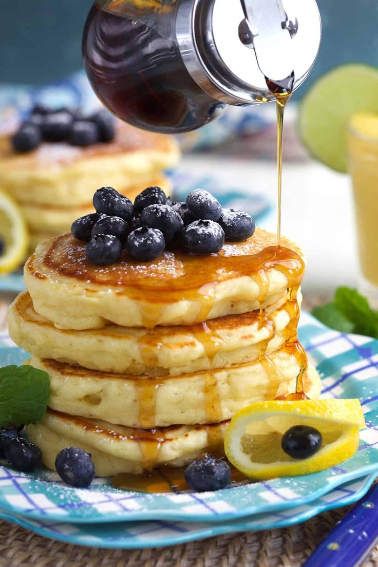 a stack of pancakes with syrup being drizzled over them and topped with blueberries