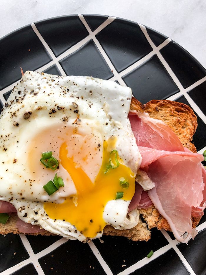 a black plate topped with an egg, ham and cheese on top of toasted bread