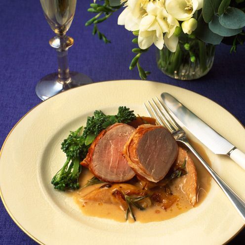 a white plate topped with meat and broccoli covered in gravy next to a glass of wine