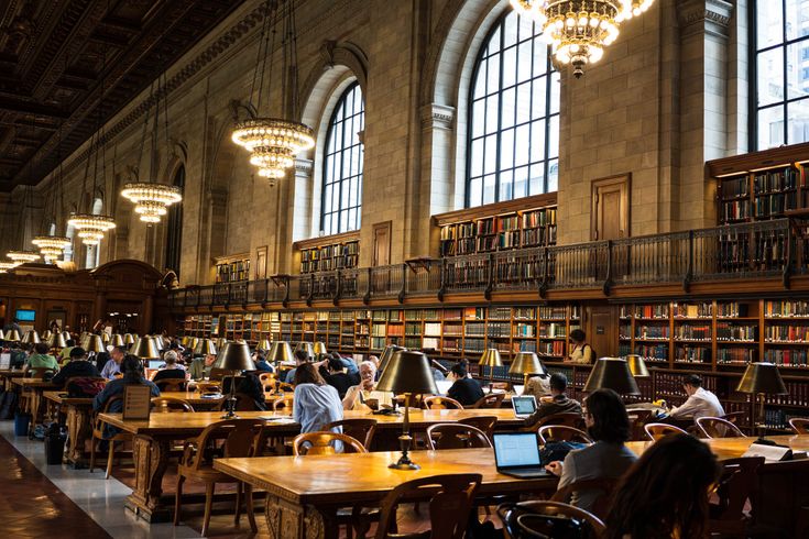 people sitting at tables in a large library with lots of bookshelves and chandeliers