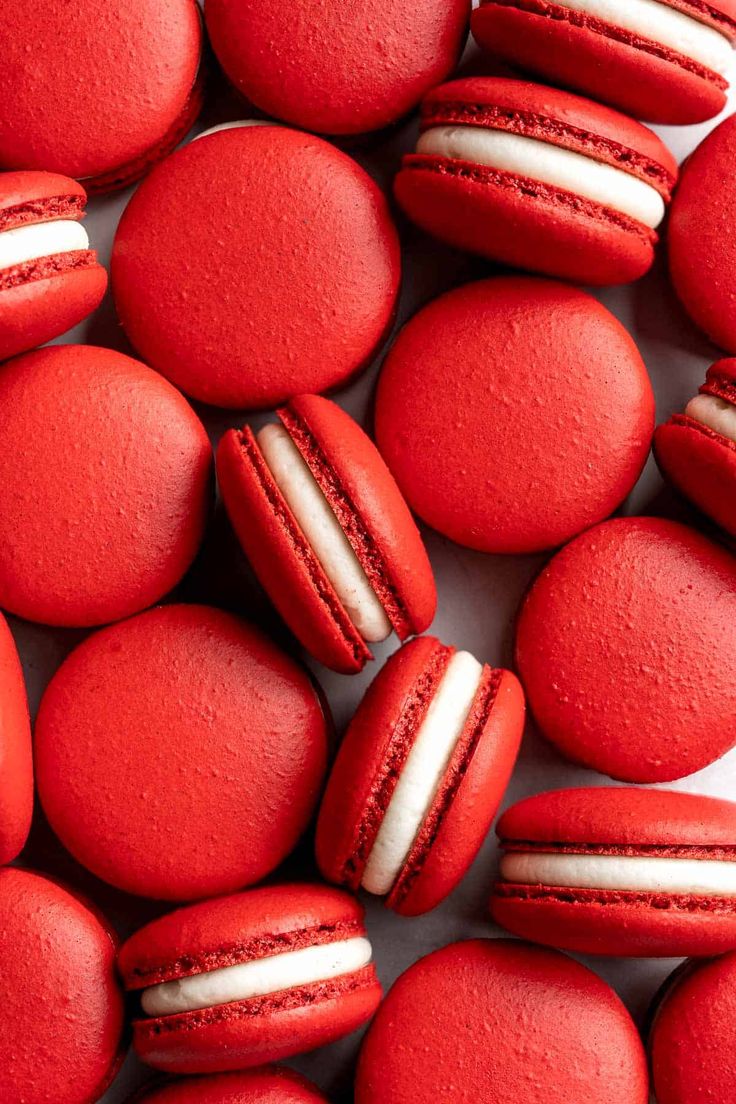 red macaroons with white frosting on them are arranged in a pile together