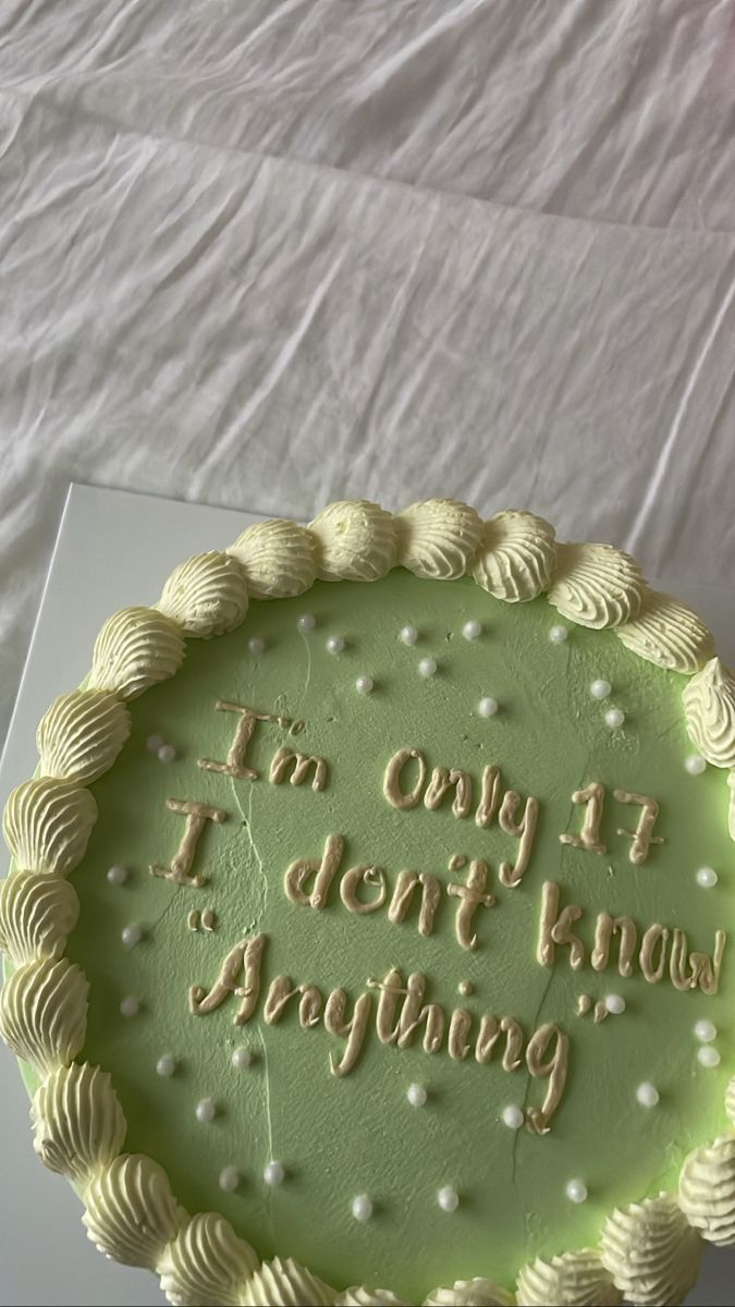 a green cake with writing on it sitting on a white tablecloth covered bed sheet