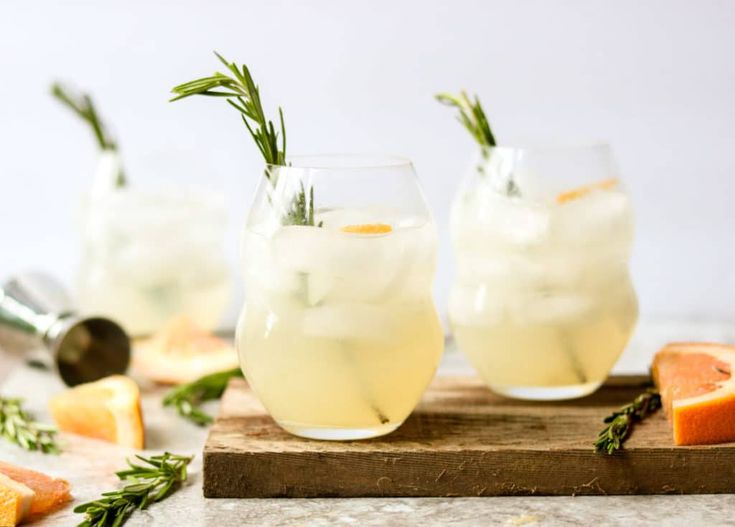 two glasses filled with lemonade and rosemary garnish on top of a cutting board