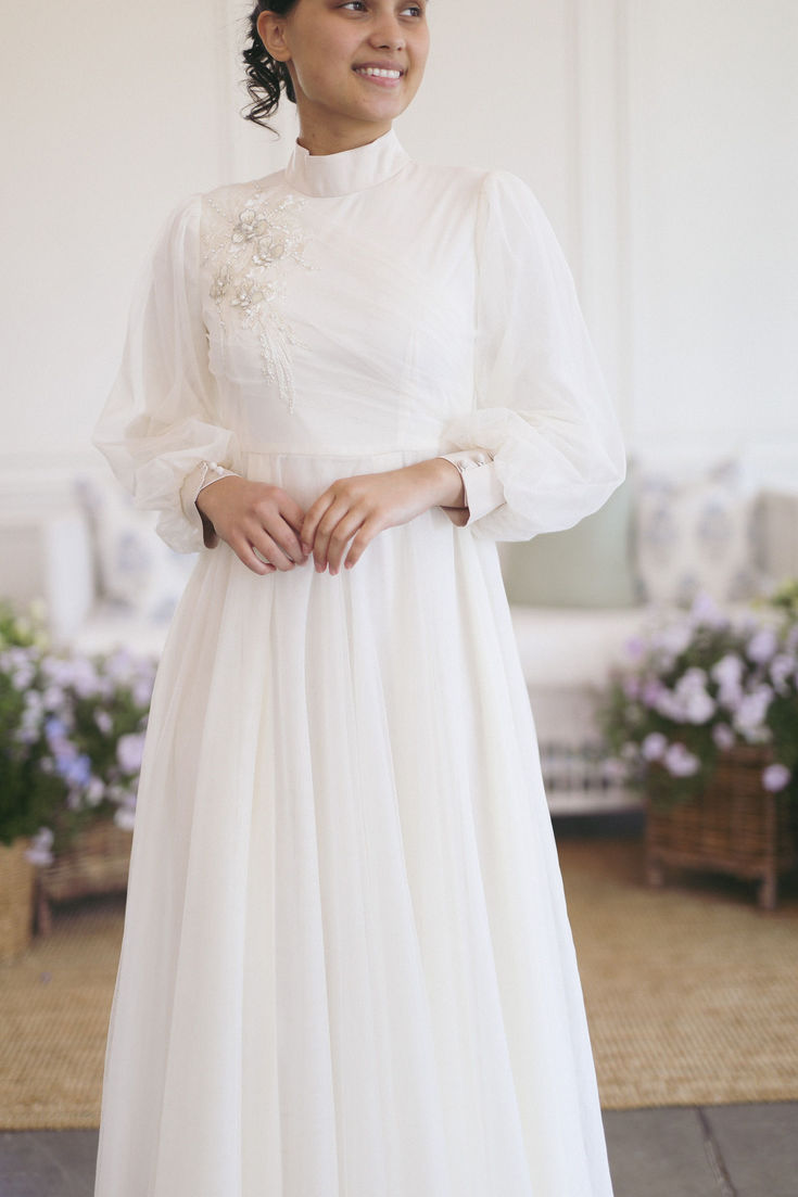 a woman in a long white dress posing for the camera with her hands on her hips