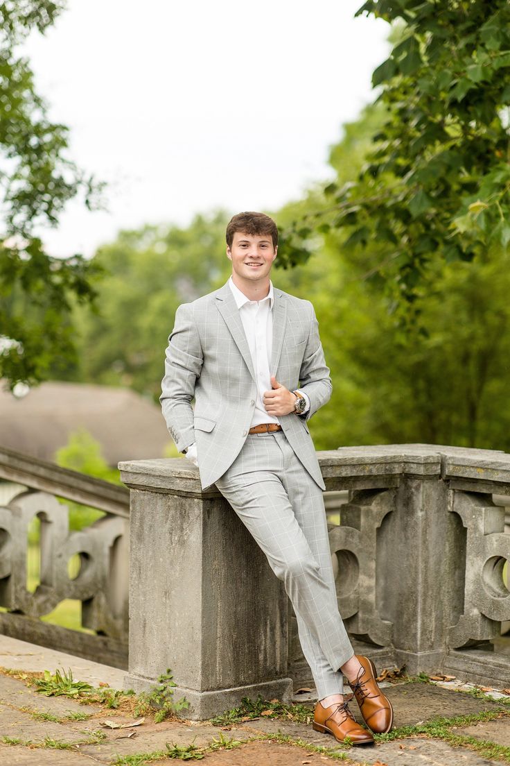 a man in a gray suit sitting on a stone wall with his legs crossed and wearing brown shoes