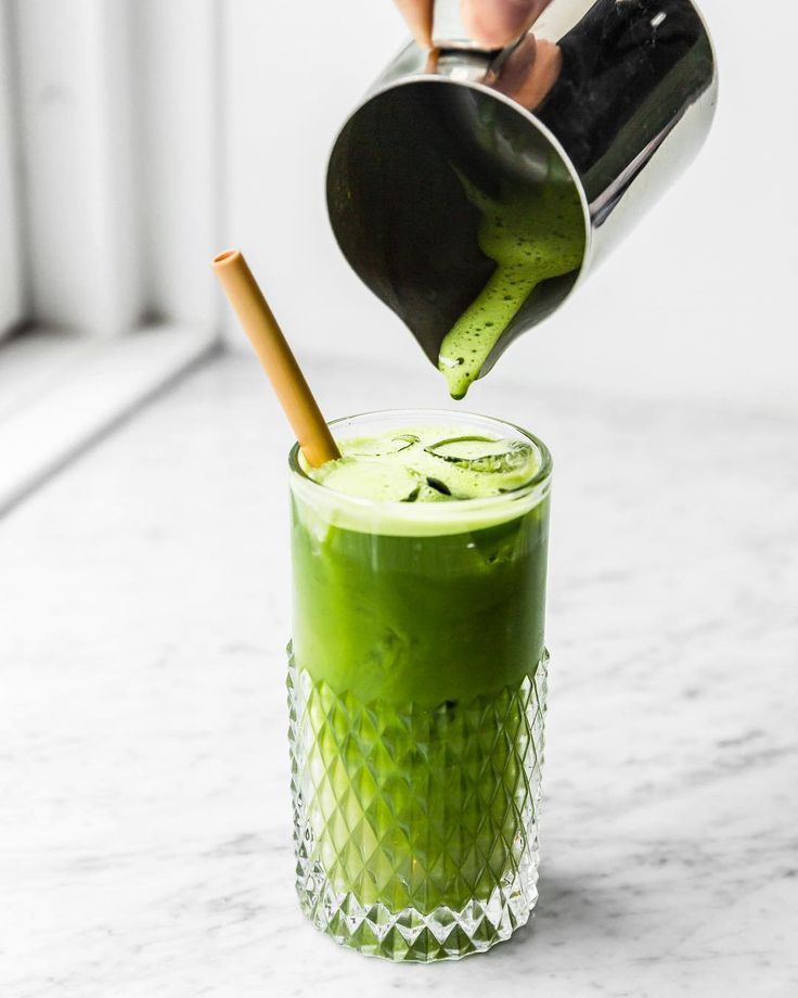 a person pours green liquid into a drink in a glass on a marble table