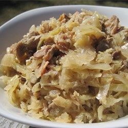 a white bowl filled with cabbage and meat on top of a wooden table next to a bottle