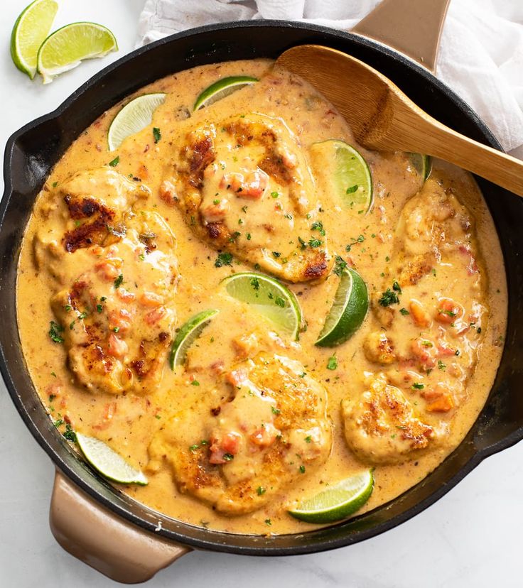 a skillet filled with chicken and cheese covered in sauce, garnished with lime wedges