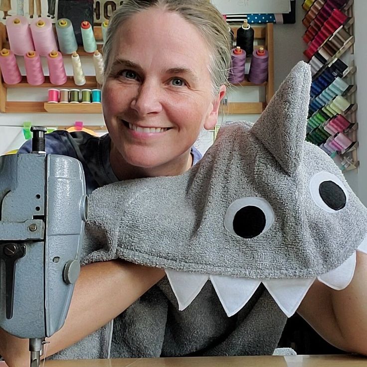 a woman is smiling while working on a sewing machine with a shark shaped pillow over her shoulder