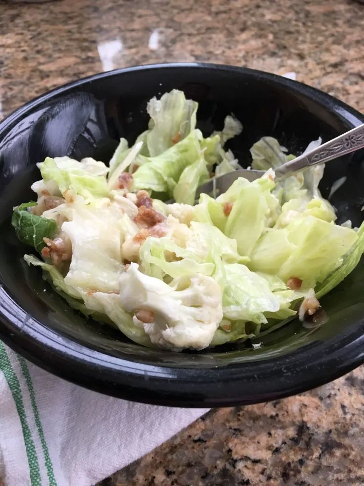 a black bowl filled with lettuce on top of a counter next to a knife