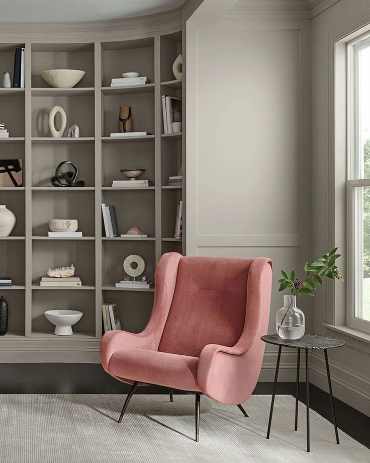 a pink chair sitting in front of a bookshelf filled with lots of shelves