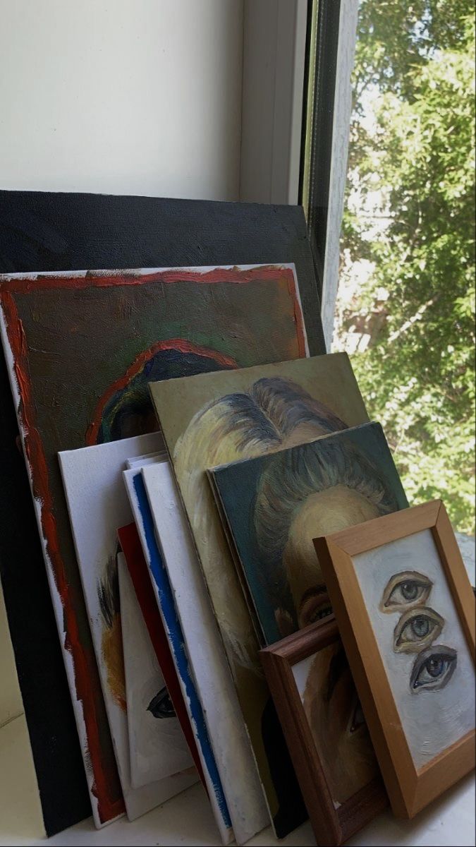 an assortment of framed and unframeed art on a window sill