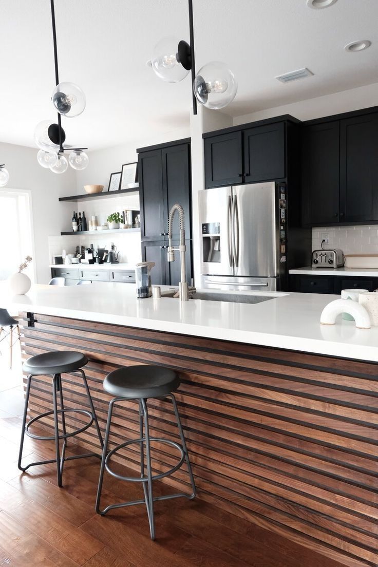 two stools sit at the bar in this modern kitchen with black cabinets and stainless steel appliances