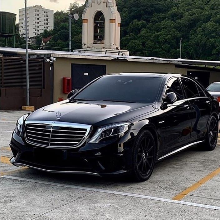 a black car parked in front of a building with a clock tower on it's side