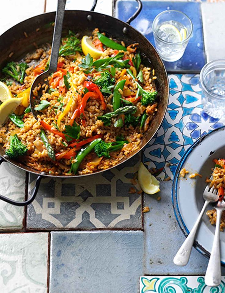 a skillet filled with rice and vegetables on top of a table next to plates