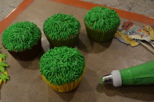 four cupcakes with green frosting and sprinkles on a baking sheet