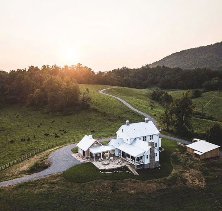 an aerial view of a white house in the middle of a green field at sunset