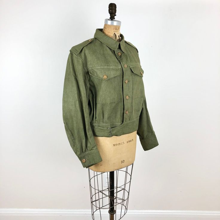 "1950s British military green cotton denim jacket has button flap chest pockets, epaulets, and a side buckle closure at the waist. The jacket has a button front and button cuffs- all of the buttons are shank buttons. Label is W.A. Phelps Ltd, dated 1954. Condition Overall very good, has tiny stains on the lright front chest above the pocket to the placket, a couple of tiny spots on the left pocket, and a spot below. Measurements Chest 46\" Waist 34\" Shoulder 18\" Sleeve length 24\" Length 23\"" Utility Denim Jacket With Button Cuffs, Classic Green Utility Jacket With Buttons, Military Style Khaki Utility Jacket With Buttoned Pockets, Military Style Cotton Utility Jacket With Button Cuffs, Utility Style Khaki Denim Jacket With Flap Pockets, Classic Green Button-up Utility Jacket, Green Utility Jacket With Buttons For Workwear, Green Utility Jacket With Snap Buttons For Work, Khaki Utility Jacket With Button Cuffs