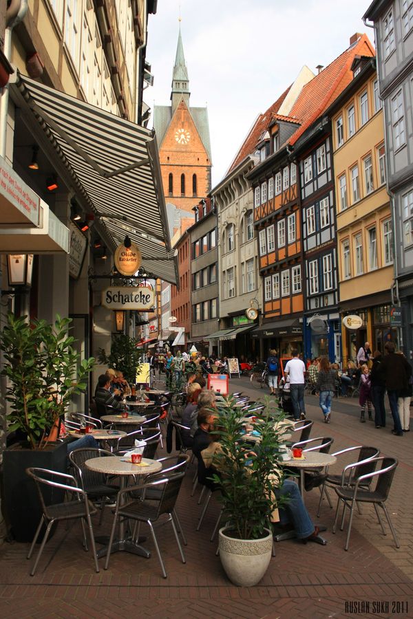 people are sitting at tables in the middle of an alleyway with buildings on both sides