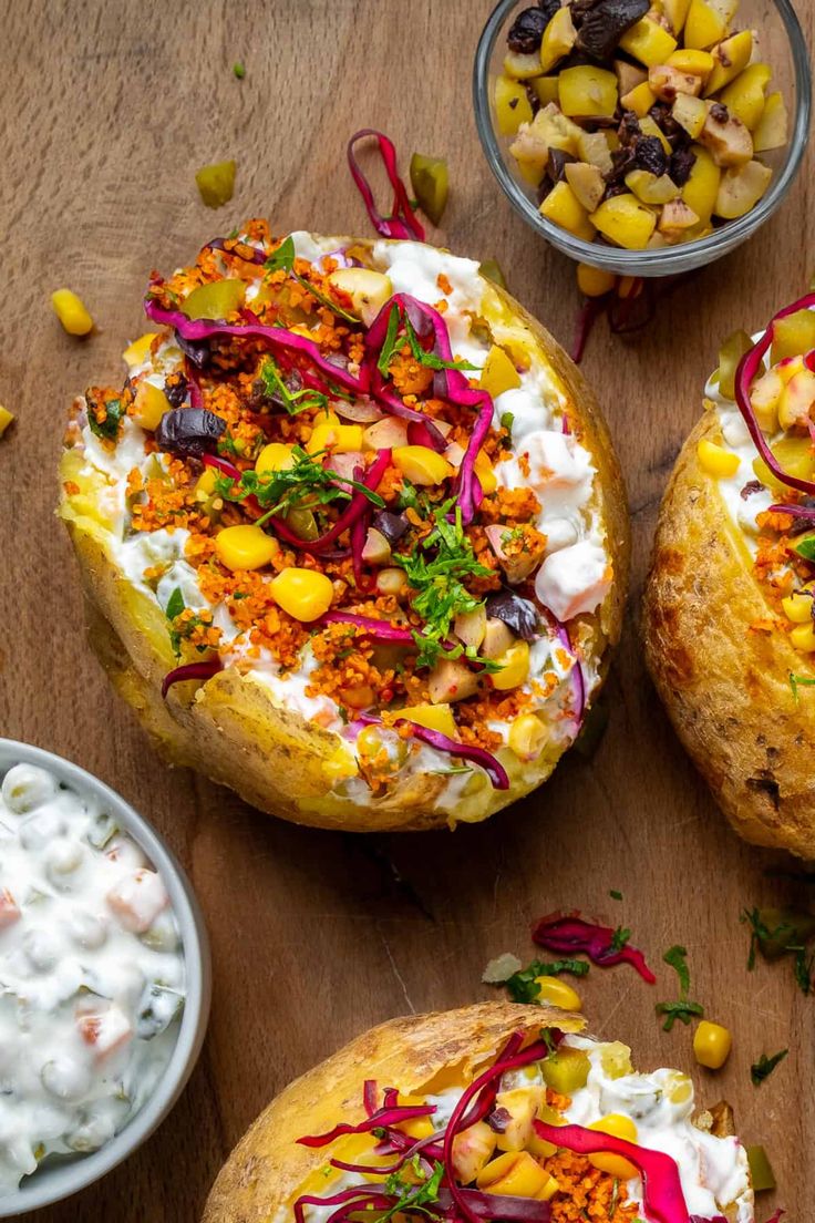 baked potatoes with colorful toppings on a wooden table next to bowls of vegetables and dip