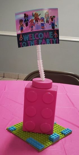 a pink table with a welcome to the party sign and legos on it's top