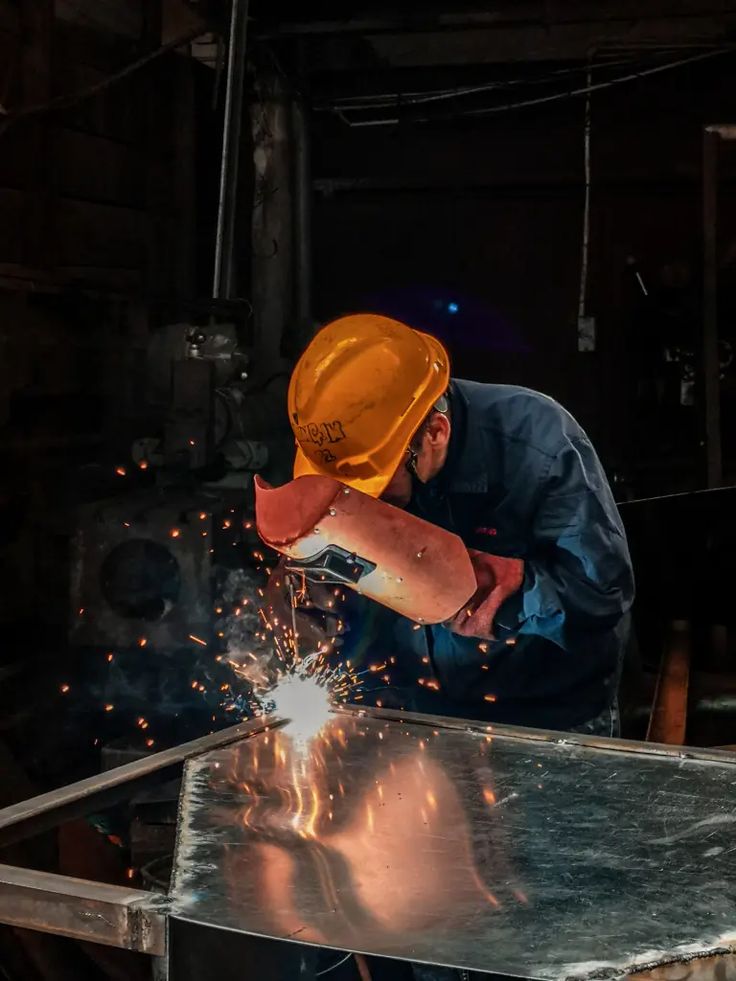 a man in an orange hard hat working on some kind of piece of metal with sparks coming out of it