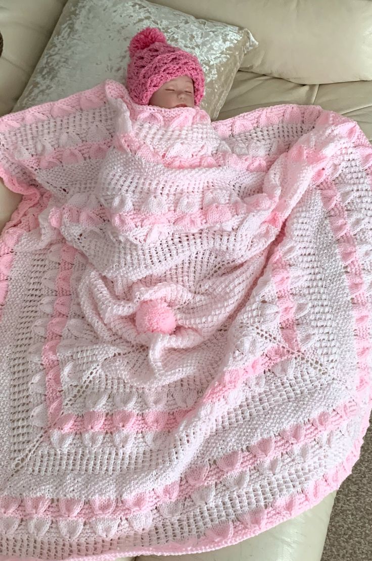 a baby wrapped in a pink and white crochet blanket on top of a couch