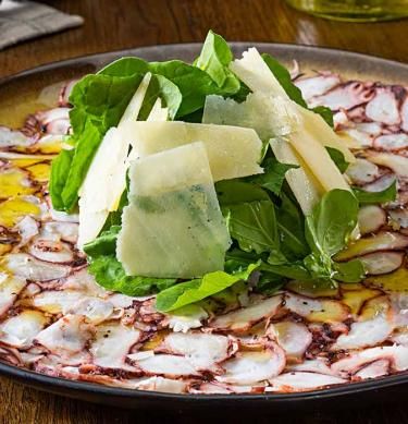 a plate topped with greens and cheese on top of a wooden table next to glasses