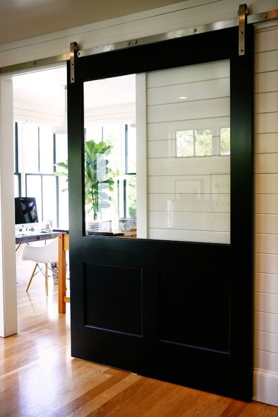 an open black door in the middle of a room with wood floors and white walls