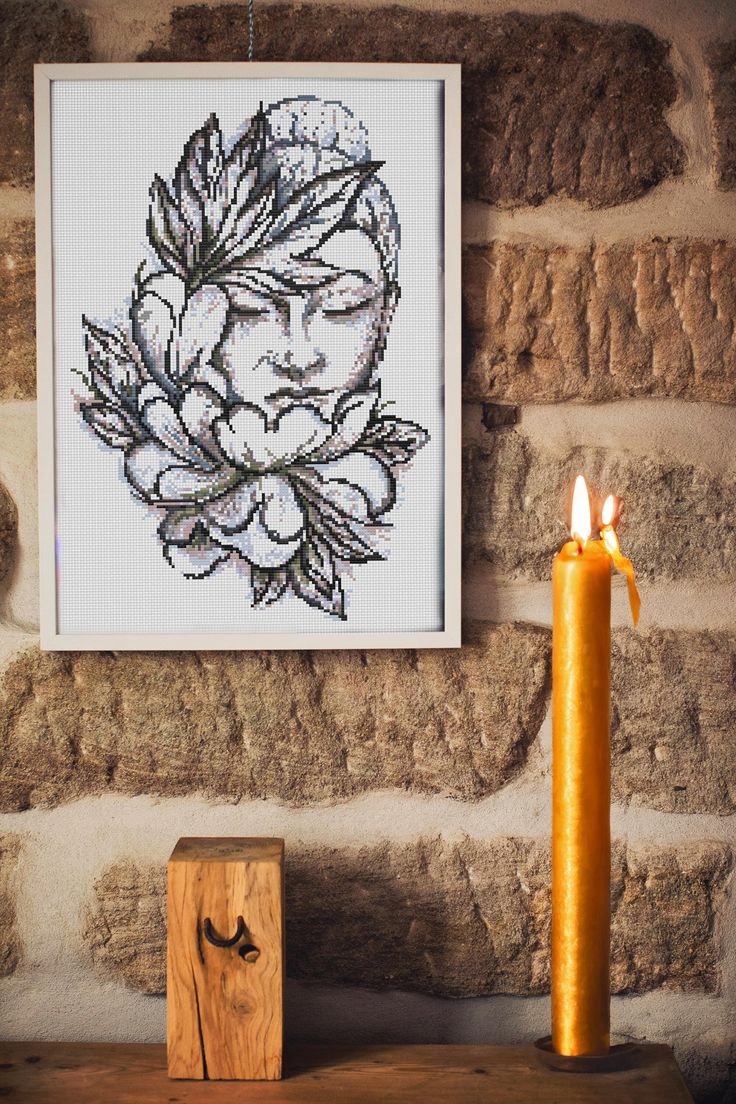 a lit candle sitting on top of a wooden table next to a framed artwork piece