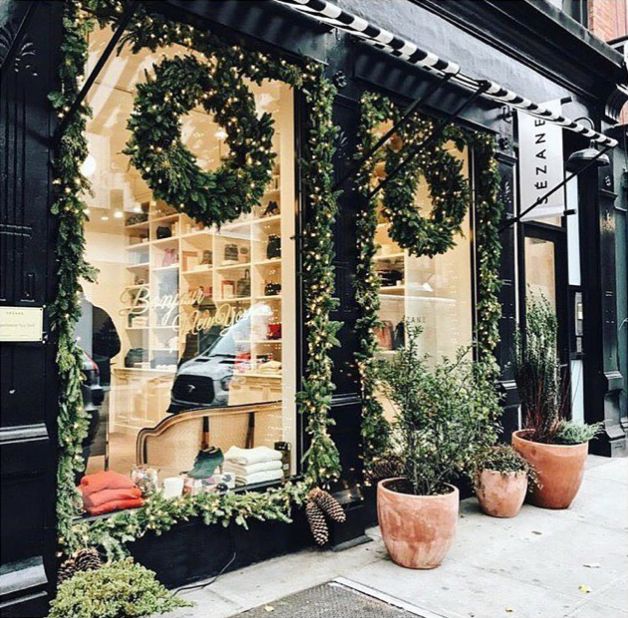 a store front with plants and potted plants in the window displays an evergreen wreath