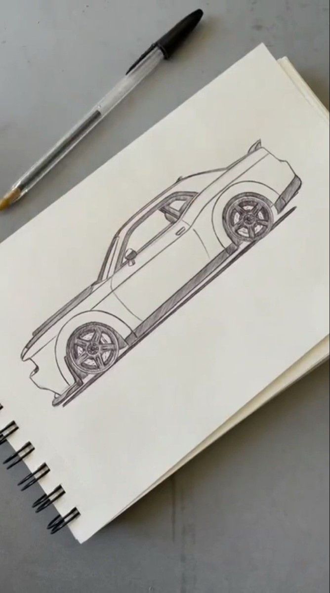 a drawing of a sports car on paper next to a pen