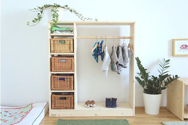 a wooden shelf with baskets and clothes hanging on it in front of a white wall