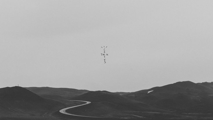 a black and white photo of a winding road in the middle of mountains with an airplane flying overhead