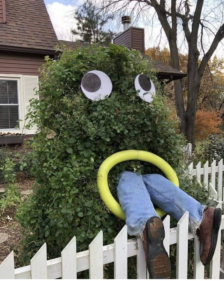 a man laying on top of a white picket fence next to a green bush with googly eyes