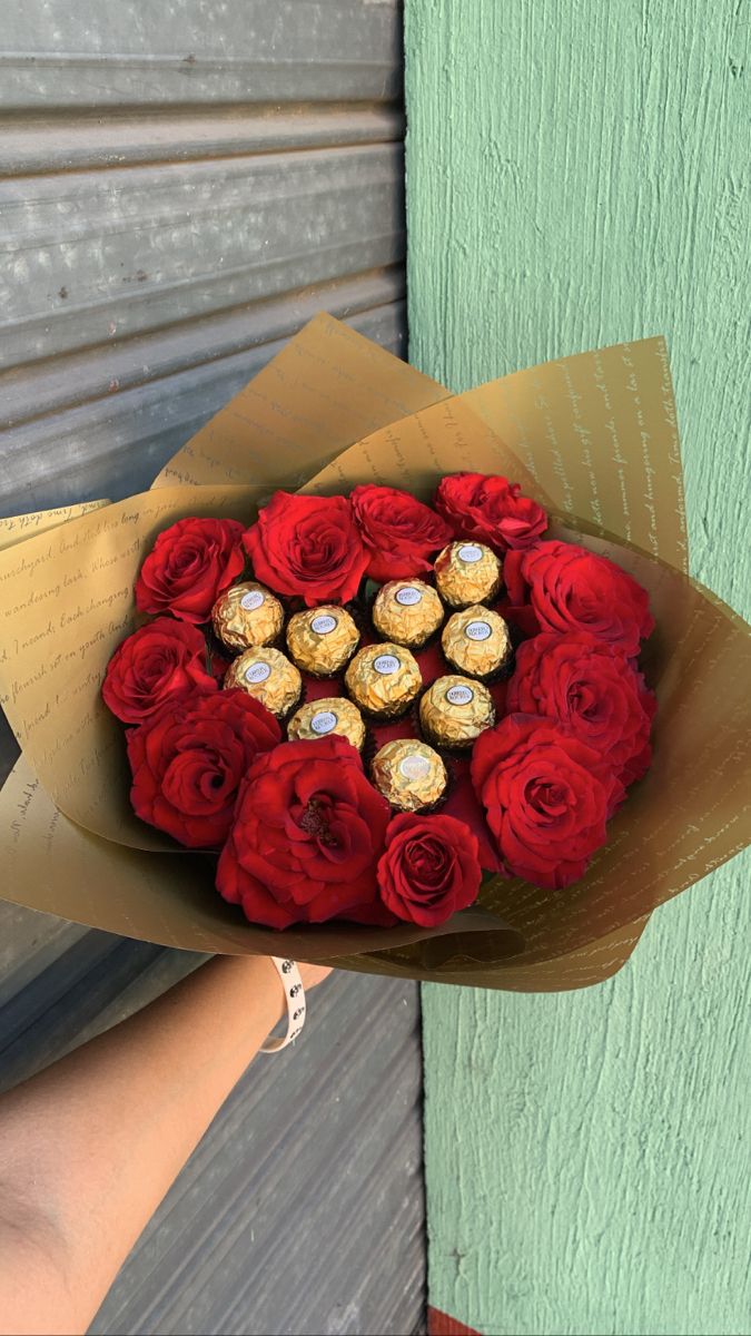 a bouquet of red roses and chocolates in a heart shaped box with someone holding it