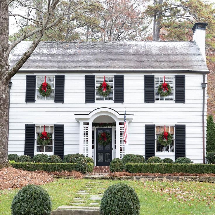 a white house with black shutters and wreaths