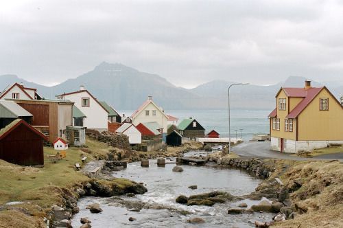 a river running through a small village with mountains in the backgroud and houses on either side